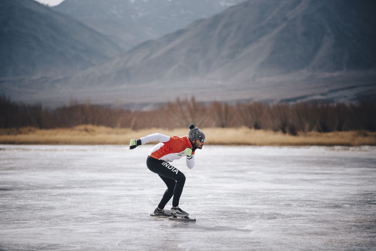Vishwaraj speed skating across a frozen lake in Ladakh, mountains behind